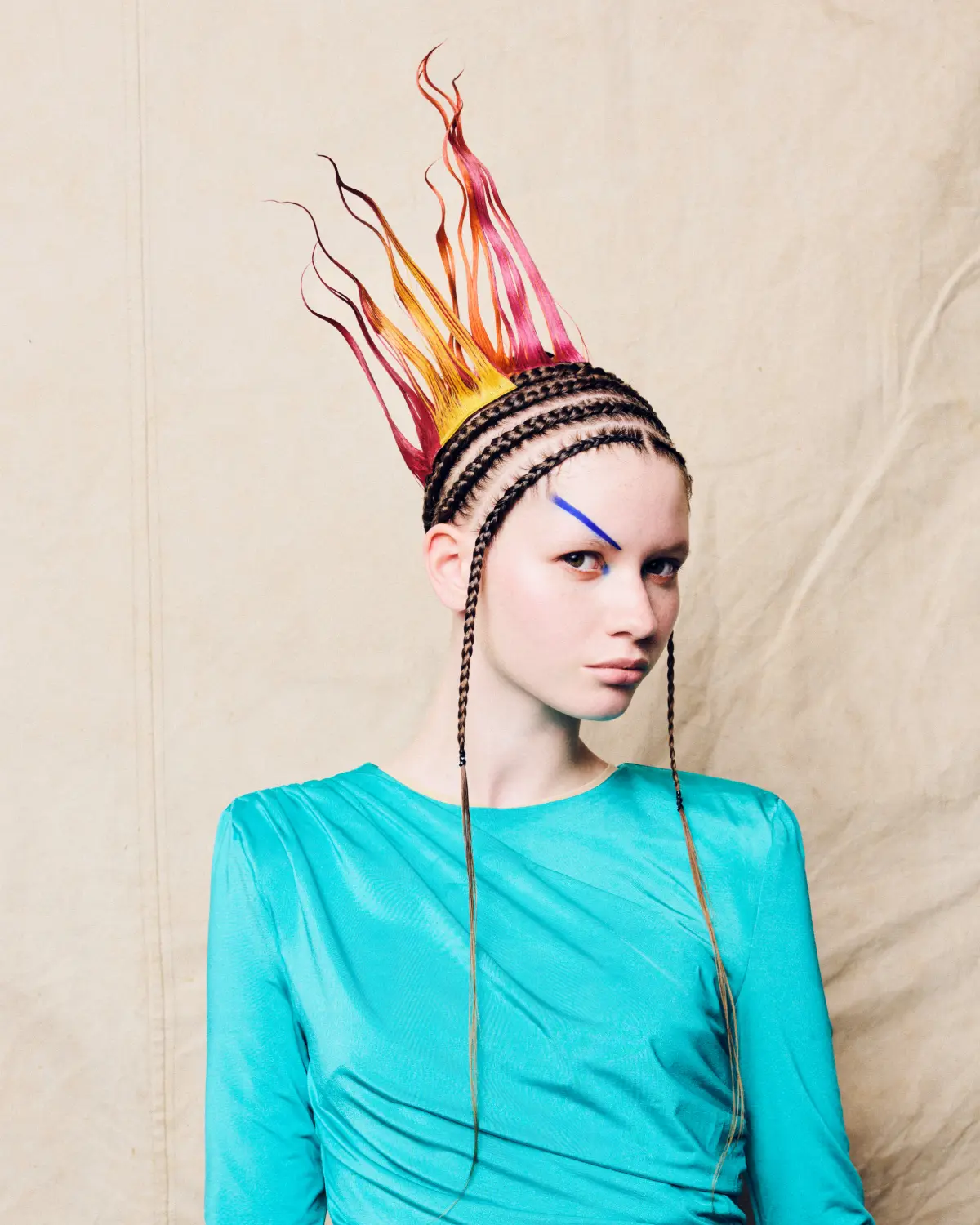 Model with braided cornrows and flame-inspired sculptural hair in vibrant orange and pink tones for an editorial hair collection.