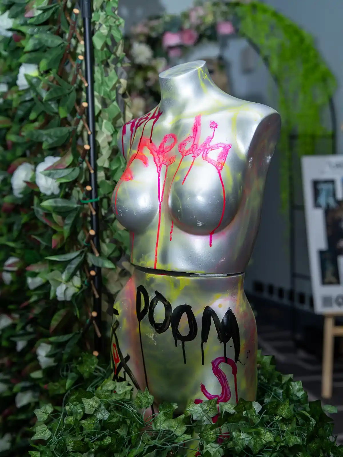 A silver mannequin decorated with graffiti next to plants on display at Never Just Hair exhibition.