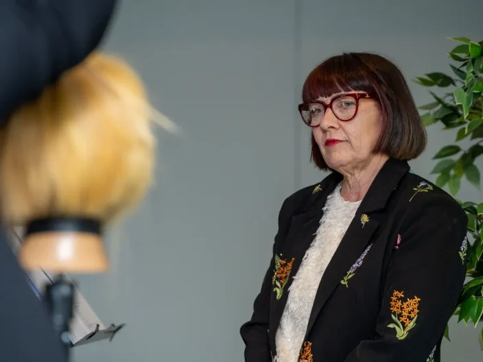 Woman with short brown hair watches a demo at Never Just Hair exhibition.