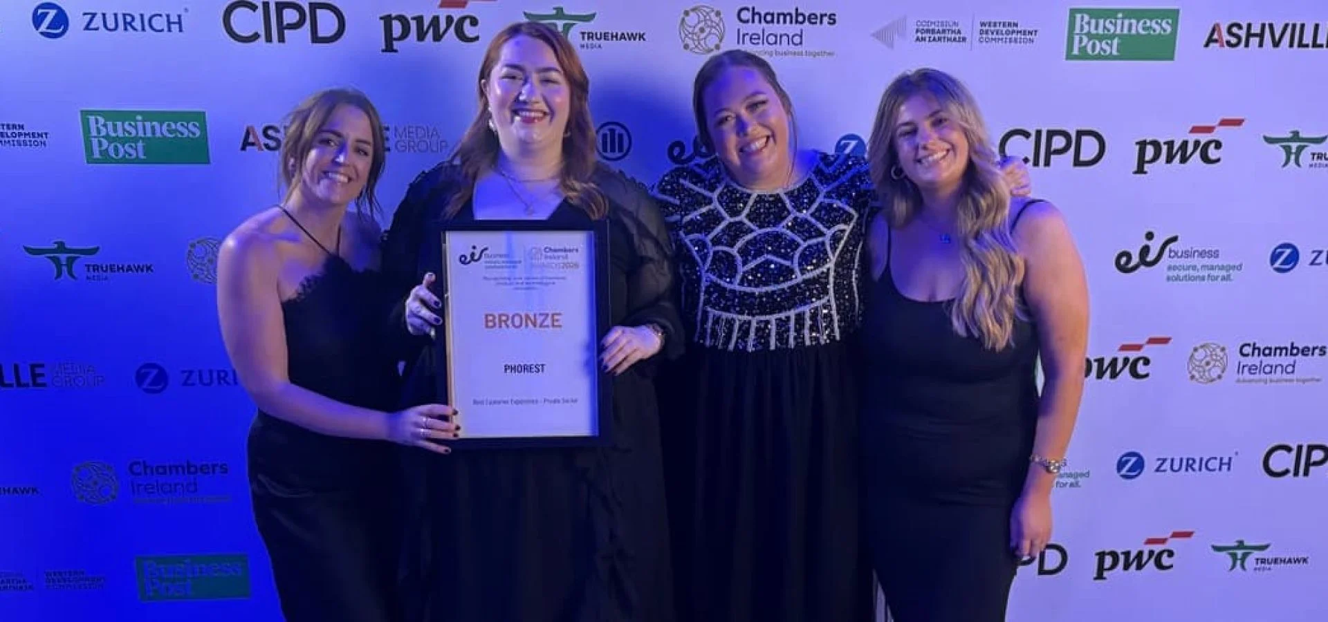 Some of the team from Phorest Salon software smile for the camera holding an award against a sponsorship board.