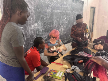Anne Veck sits in front of a chalk board In Uganda teaching students hair skills.