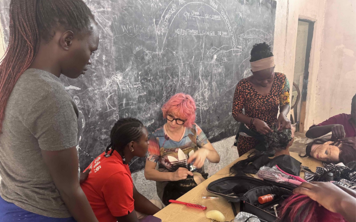 Anne Veck sits in front of a chalk board In Uganda teaching students hair skills.