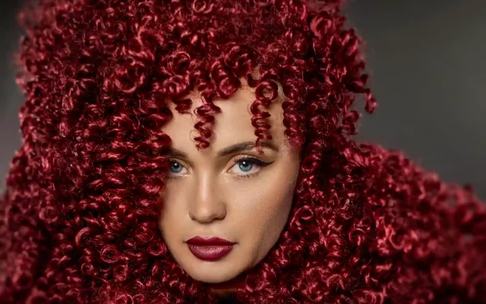 Model with long, red flowing curls all over her head and shoulders from the Marlene Lamont Conviction Collection.
