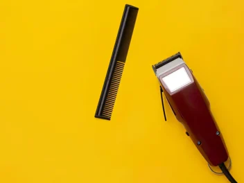 A Barber's trimmer next to a comb on a yellow background.