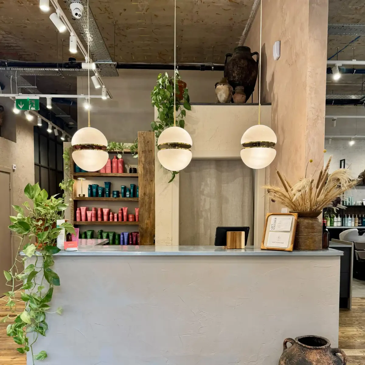 Butchers Salon reception featuring reclaimed wood, indoor plants, natural décor and sustainable salon design with Aveda retail display.
