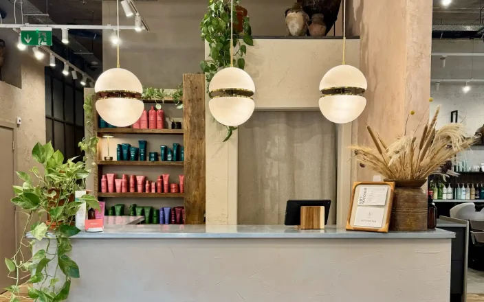 Butchers Salon reception featuring reclaimed wood, indoor plants, natural décor and sustainable salon design with Aveda retail display.