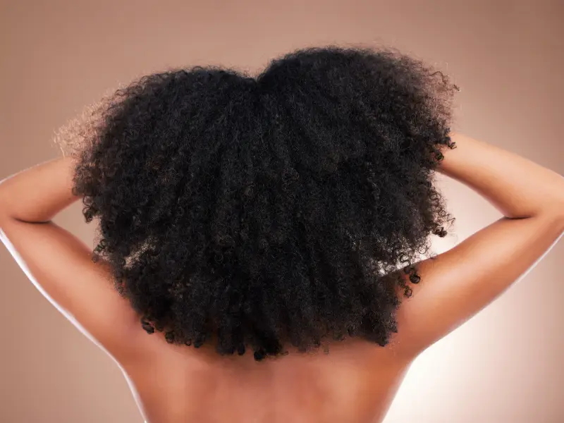Curly hair model stands with her back to the camera and hands in her hair.
