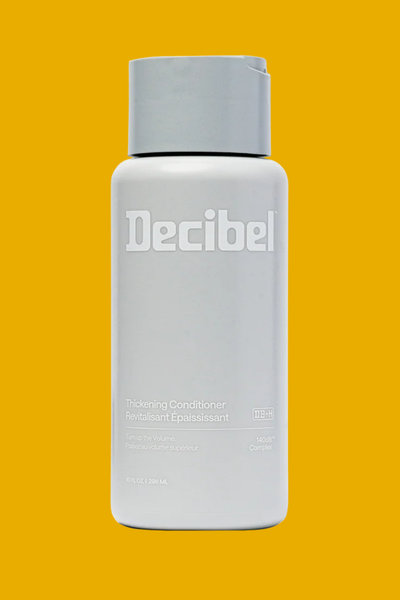 A branded grey bottle of Decibel Conditioner on a yellow background.