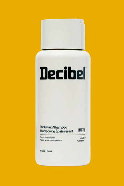 A black and white branded bottle of Decibel Shampoo on a yellow background.