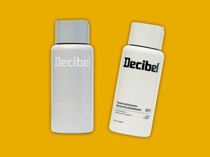 A bottle of Decibel Shampoo and a bottle of Decibel Conditioner on a yellow background.