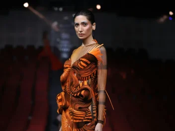 Model with slicked back hair and blue eyebrows on stage highlighting the F.A.M.E. Team finals.