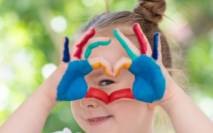 Happy child smiles and makes a kind love heart shape.