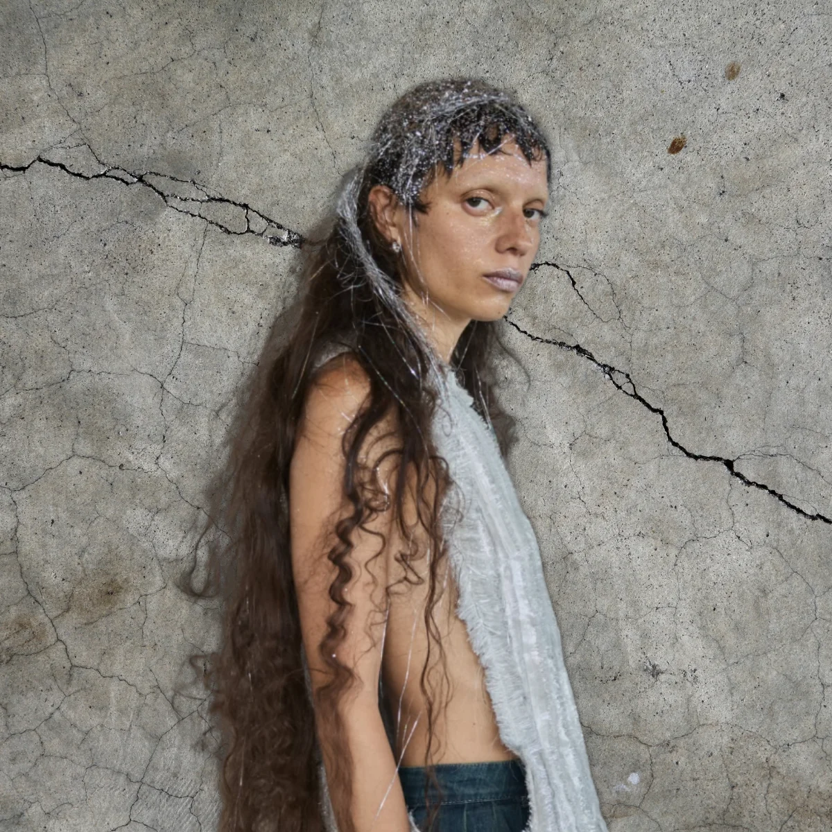 Model at Copenhagen Fashion Week with tinsel in her hair against a concrete backdrop.