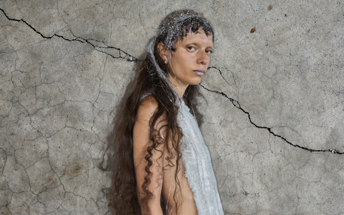 Model at Copenhagen Fashion Week with tinsel in her hair against a concrete backdrop.