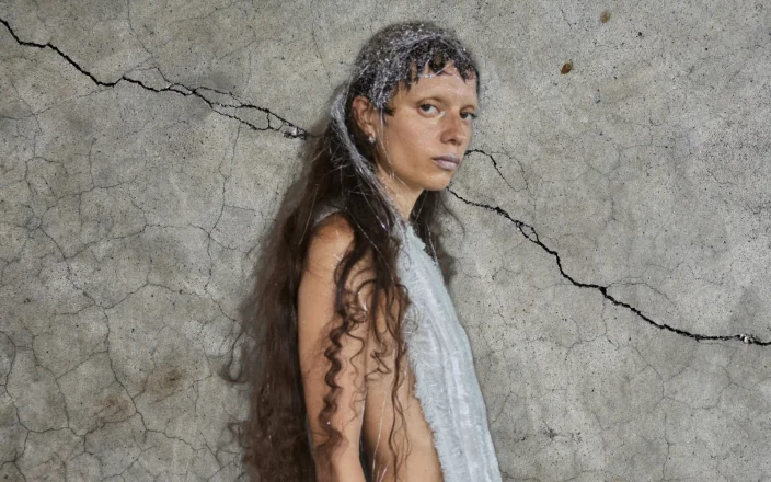 Model at Copenhagen Fashion Week with tinsel in her hair against a concrete backdrop.