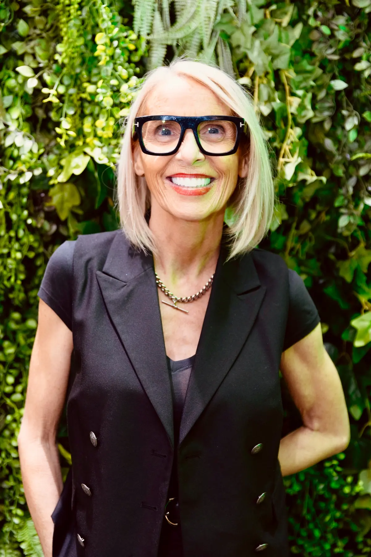 Marlene Lamont smiles for the camera in front of a hedge.