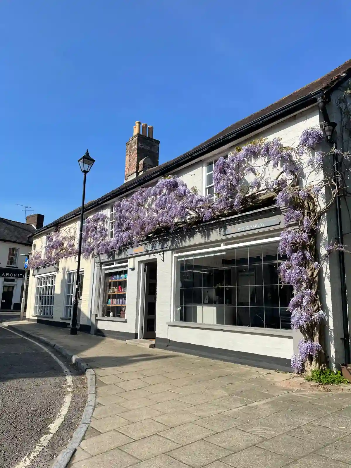 A white building that is Pare Hair Salon with lilac plants climbing its walls.