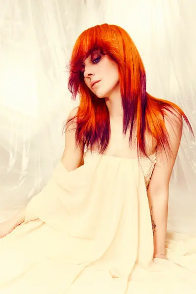 A model with vibrant orange and red flowing hair from the Solstice collection by Safy Burton, inspired by the shifting tones of sunrise and sunset skies with soft movement, luminous colour and atmospheric tones.