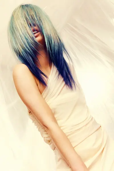 Model with long, layered blue and pale blonde hair partially covering the face from the Solstice collection by Safy Burton, featuring fluid movement and luminous cool tones inspired by the shifting colours of sunrise and sunset skies.