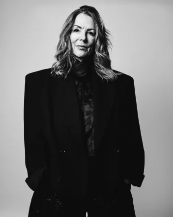 A black and white image of Suzie McGill with wavy hair and an oversized black blazer.