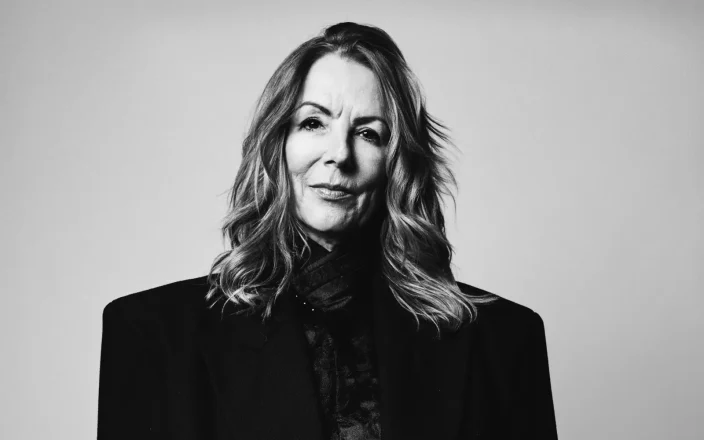 A black and white image of Suzie McGill with wavy hair and an oversized black blazer.