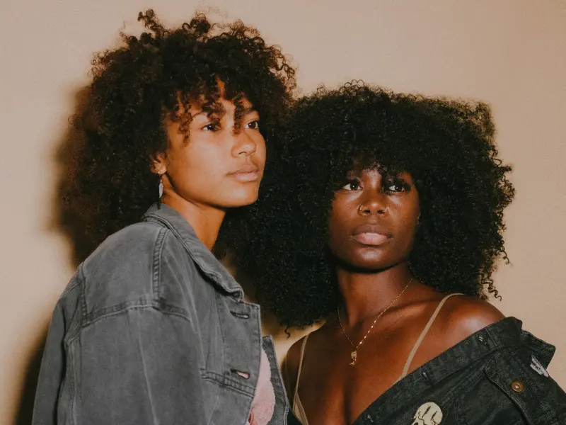 Two curl hair models stand side by side in denim.