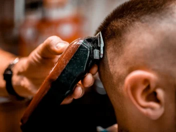 A hand holding an electric razor shaves a buzz cut on a model.