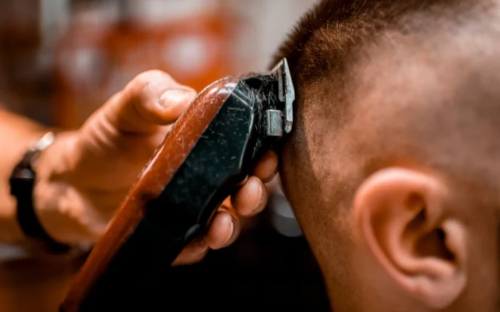 A hand holding an electric razor shaves a buzz cut on a model.