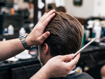 Male model's hair in a barber shop's chair with a hand holding a comb.