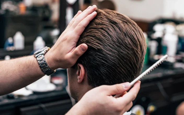 Male model's hair in a barber shop's chair with a hand holding a comb.