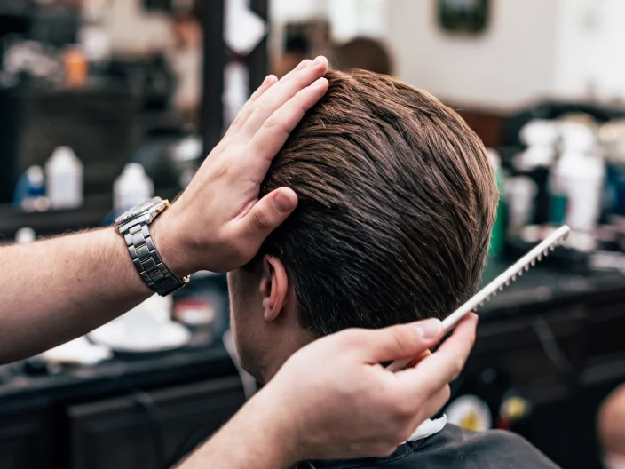 Male model's hair in a barber shop's chair with a hand holding a comb.
