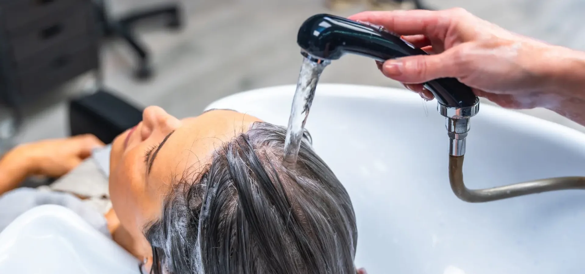 Woman at a salon backwash with a hairdresser's hand holds the tap over her hair.