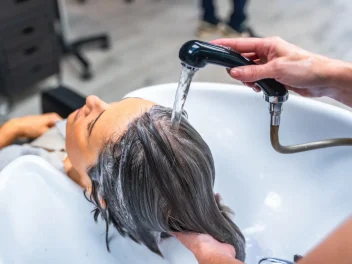 Woman at a salon backwash with a hairdresser's hand holds the tap over her hair.