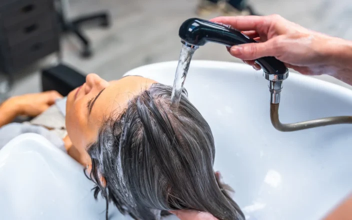 Woman at a salon backwash with a hairdresser's hand holds the tap over her hair.