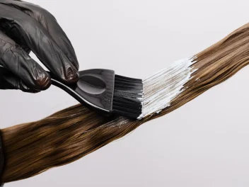 A hand paints hair with dye.