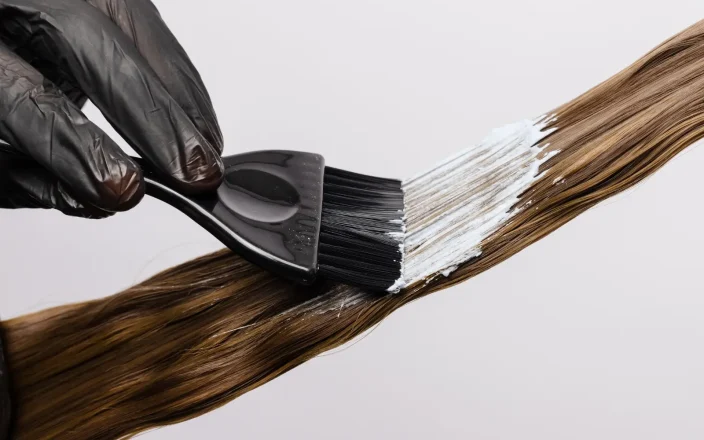 A hand paints hair with dye.