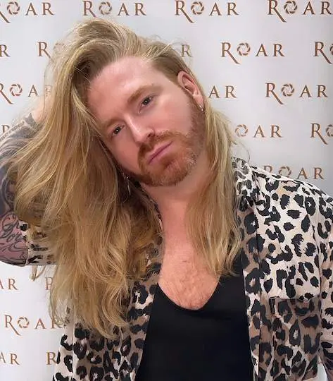 Brian Leo McCallum of ROAR Hair & Beauty in front of a branded wall.