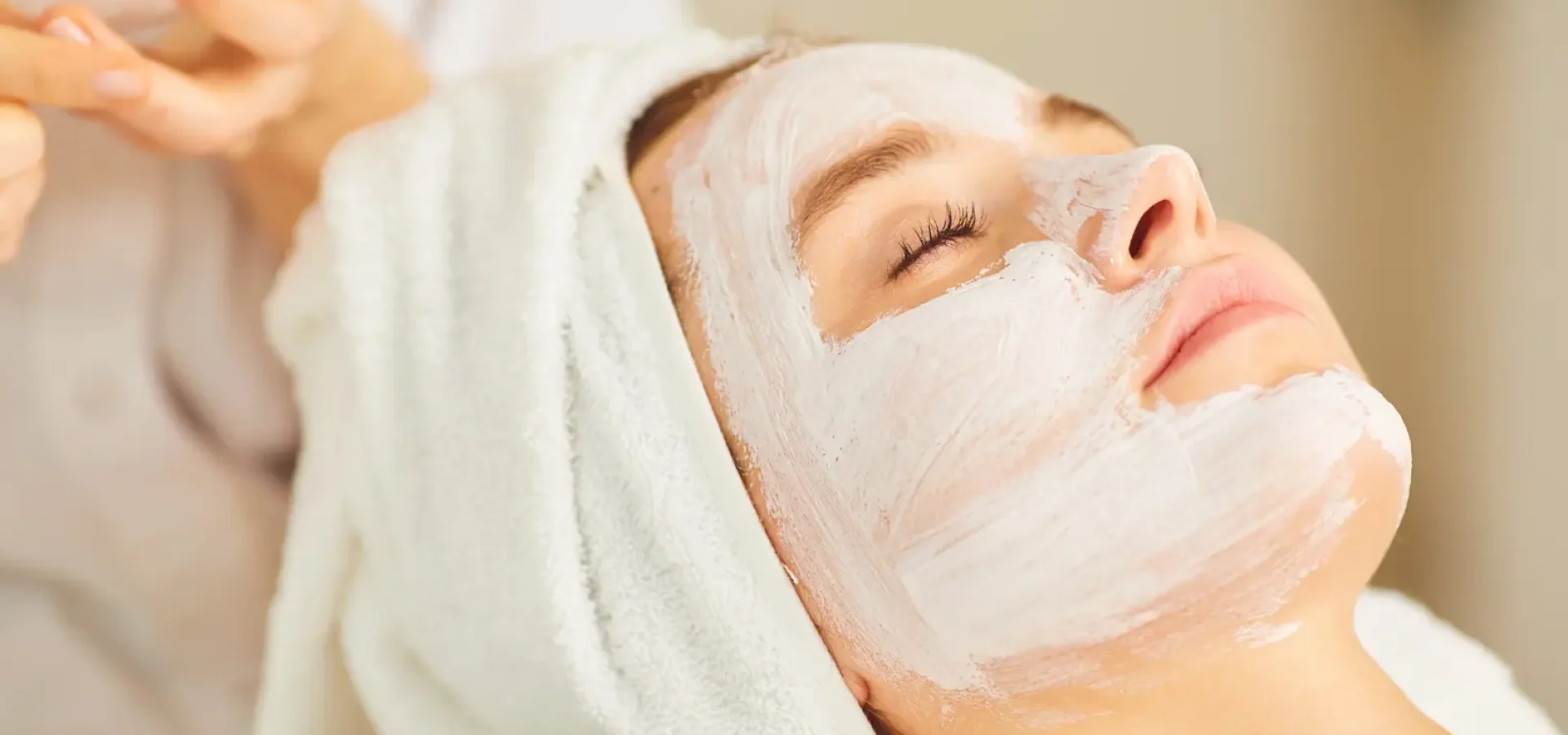 A client in a salon with a face mask and hair towel.