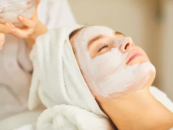 A client in a salon with a face mask and hair towel.