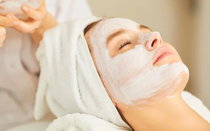 A client in a salon with a face mask and hair towel.