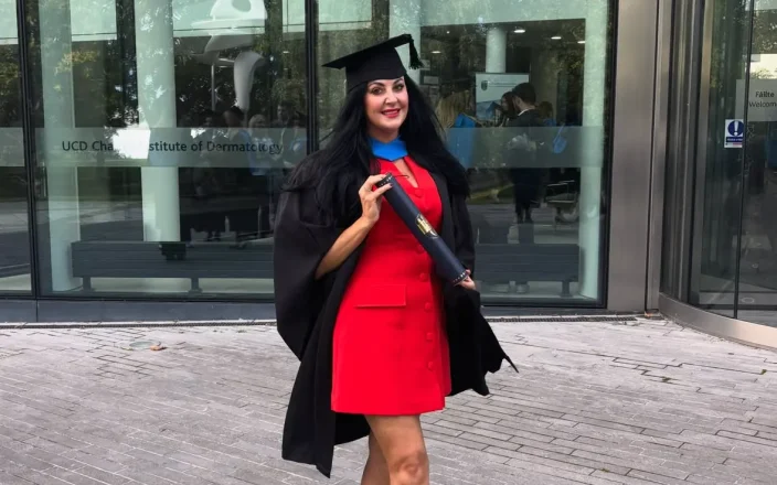 Bridgeen King stands outside a building wearing a graduation hat and holding a scroll.