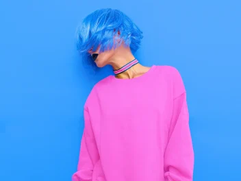 Model with blue hair and pink top turning to the side.
