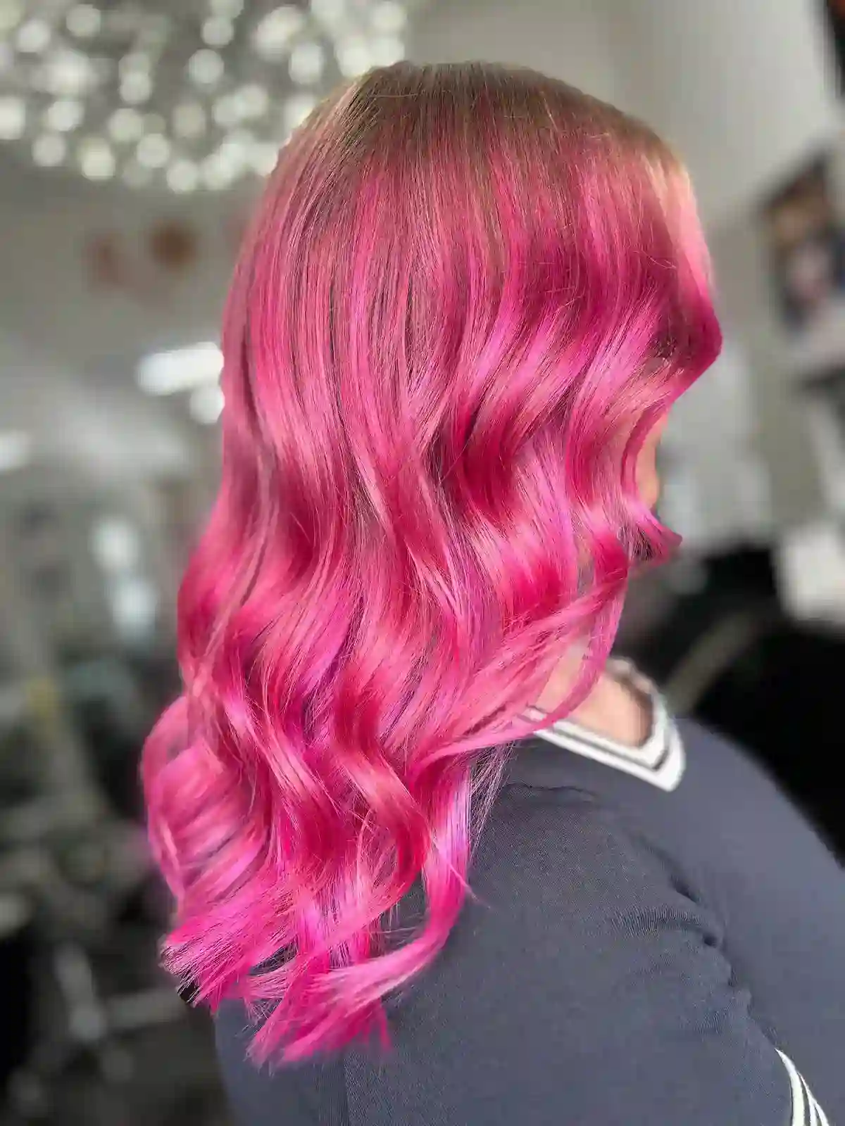 Model with blended vibrant pink into the natural roots with loose curls revealing the different pink tones as they catch the light.