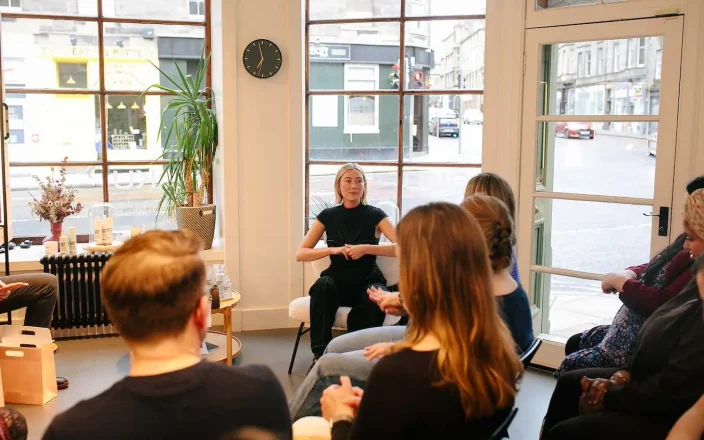 woman sits at the centre of a circle giving a talk.