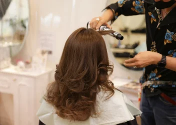 woman sits in salon chair as a hairdresser curls her hair.