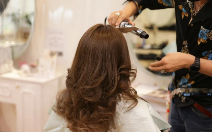 woman sits in salon chair as a hairdresser curls her hair.